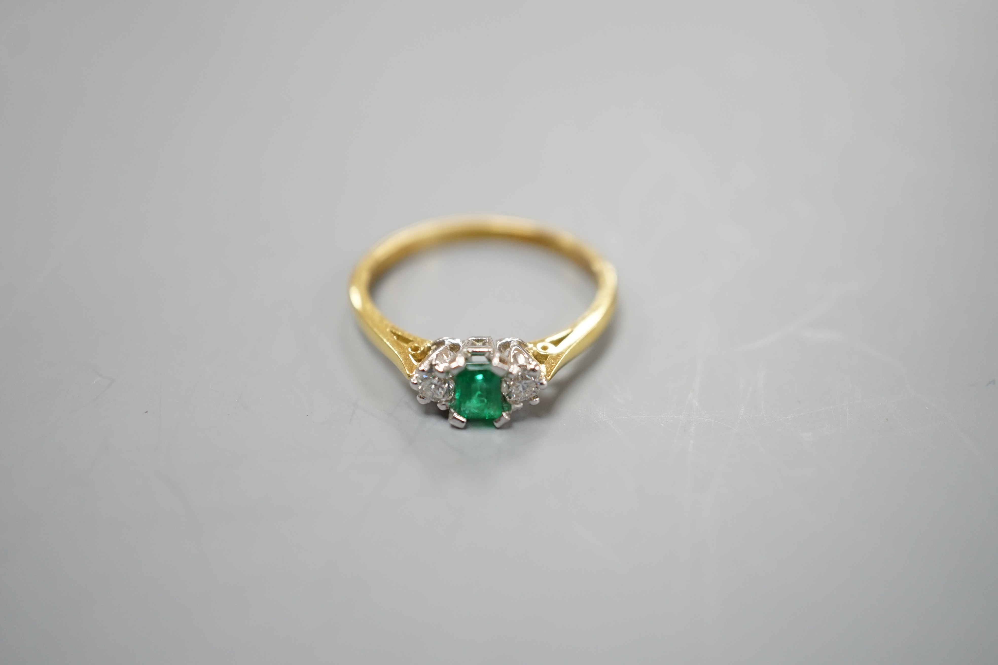 A modern 18ct gold, emerald and diamond set three stone ring, size N, gross weight 2.6 grams.